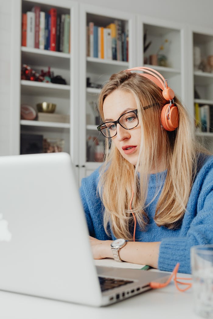 Focused woman in glasses and headphones using a laptop at home office.